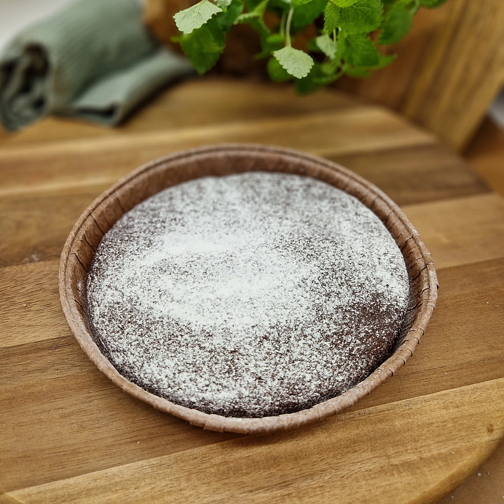 Kladdkaka med florsocker på träbricka. Mjuk kaka, fika på fikabord