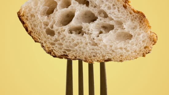 En skiva bröd på en gaffel. Gul bakgrund.