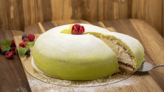 En tårtbit lyfts ur en grön prinsesstårta med röd ros.