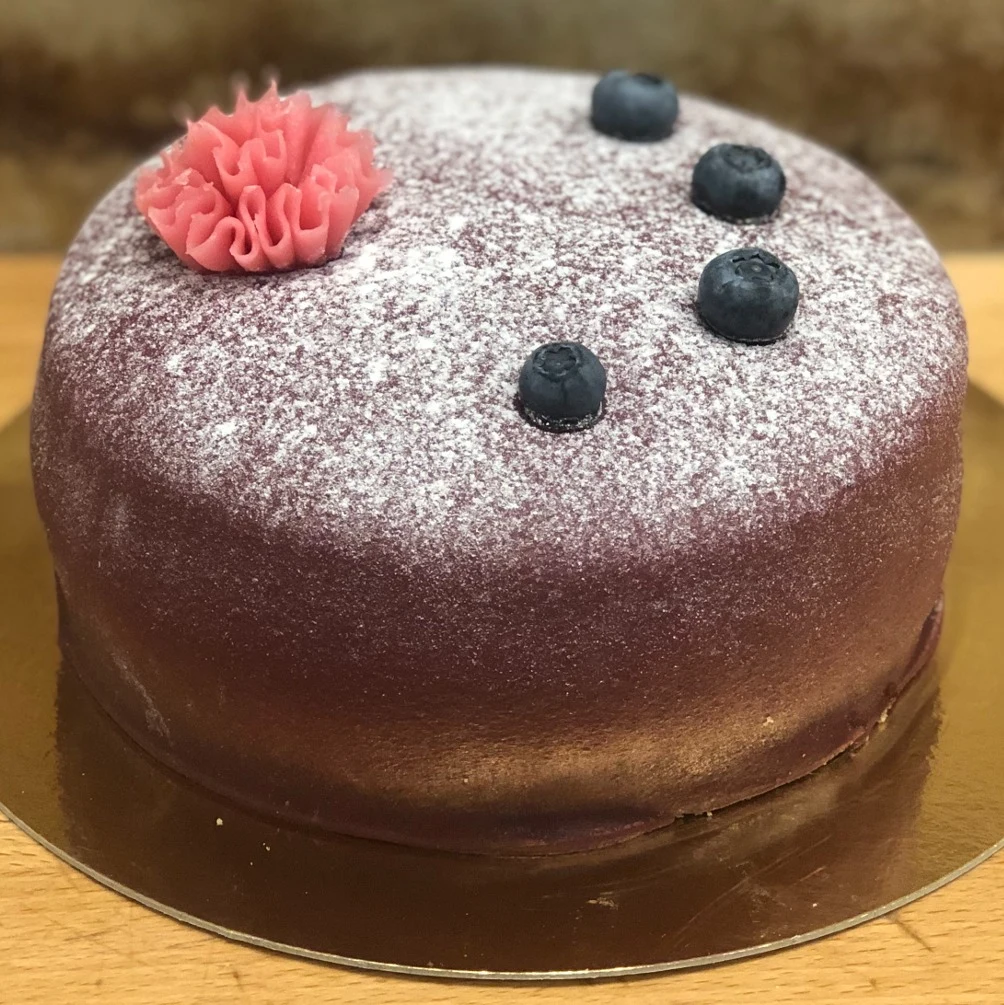 En lila prinsesstårta dekorerad med blåbär och en rosa nejlika.