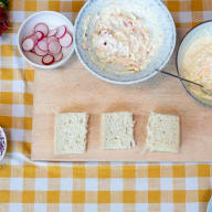 En bricka med bröd, skålar med sallad och pålägg står på en rutig duk.