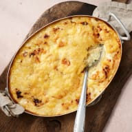 Sked tar upp en portion potatisgratäng ur en ugnsform.