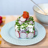 En tallrik med en rätt bestående av skivad rädisa, hackad persilja och en topp av kaviar serveras på ett träbord.