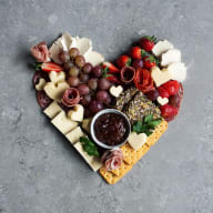 Ost, kex, vindruvor, jordubbar, marmelad ligger uppdukat på en bricka i formen av ett hjärta.