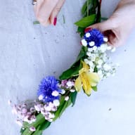 En person arrangerar blommor och blad till en krans på ett tyg.