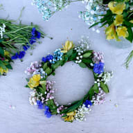 En blomsterkrans ligger på en yta med andra blommor och växter runtomkring.