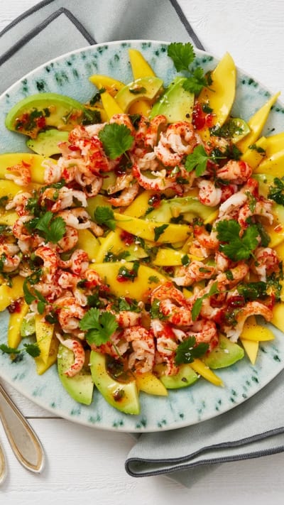 Skivad mango och avokado på ett stort fat, toppat med kräftstjärtar, chili, koriander och dressing.