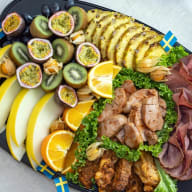 svart serveringsfat med skivade frukter och kött men den liten svensk flagga