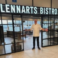 En person står framför ingången till ett bistro med utsträckta armar.