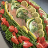 Serveringsfat med hel lax garnerad med citronskivor, gurka, dill, sparris och jordgubbar.