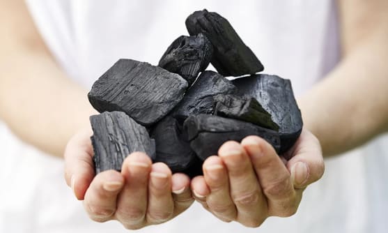Kupade händer håller i svarta block med grillkol