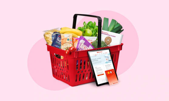 En varukorg som är fylld med mat. Bredvid står en ipad med ICA-appen på skärmen och ett ICA-kort.