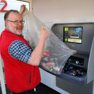 En person tömmer en påse med flaskor och burkar i en pantautomat.