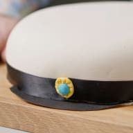 En huvudbonad med vit överdel och mörkt band ligger på en träyta.