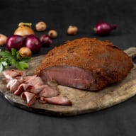 Tunnt skivad rostbiff på en träskärbräda med lök och persilja i bakgrunden.