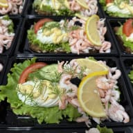 Flera räksmörgåsar toppade med ägg, dill och citronskiva på salladsblad.