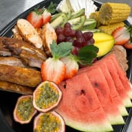 BBQ-planka med fläskfilé, kycklingfilé, kamben, majskolvar, kökets barbequesås, coleslaw, brie, vattenmelon, passionsfrukt, vindruvor, mango, kiwi och jordgubbar.