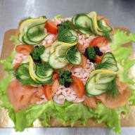 Smörgåstårta toppad med räkor, kaviar, lax, skivad gurka, tomat och dill.