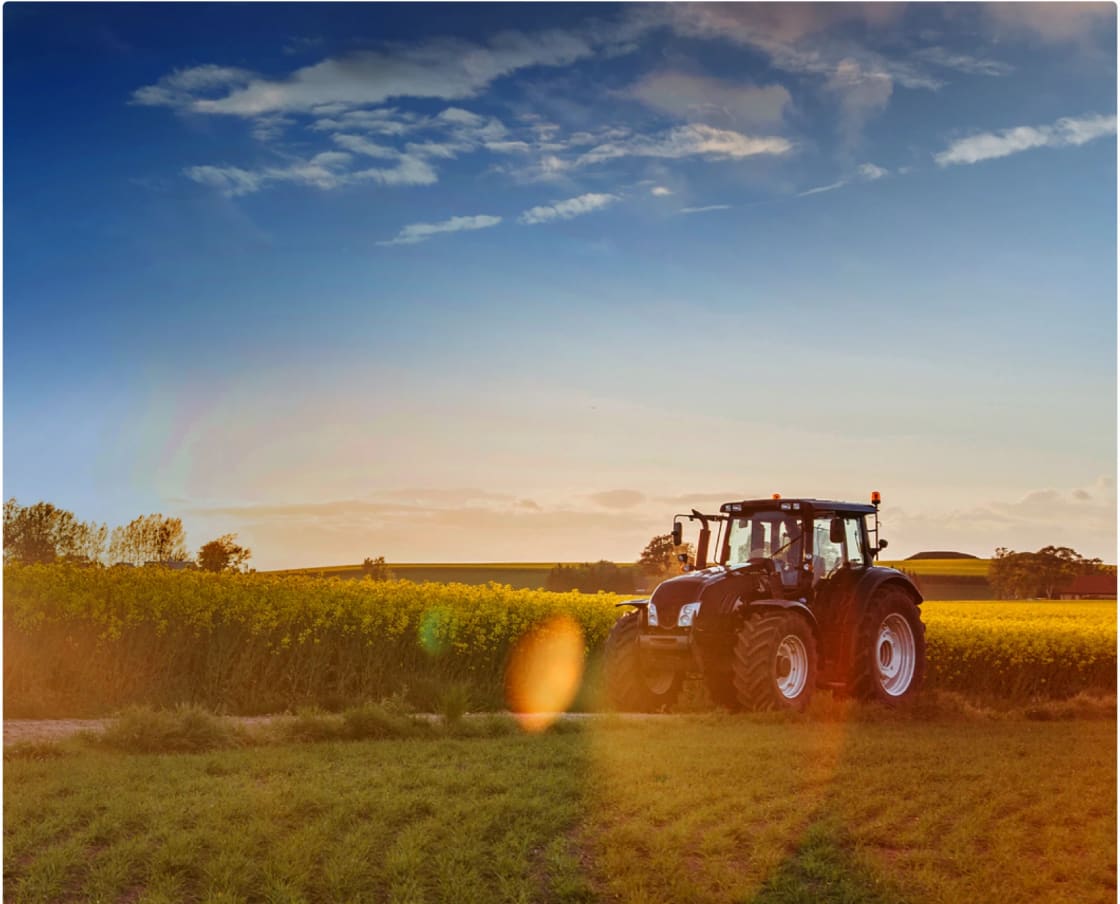 En traktor står på ett fält med träd i bakgrunden och moln på himlen.