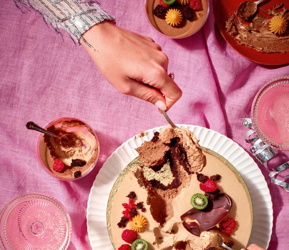 En hand som skär ut en bit av en dekorativ desserttårta på ett bord med flera små desserter.
