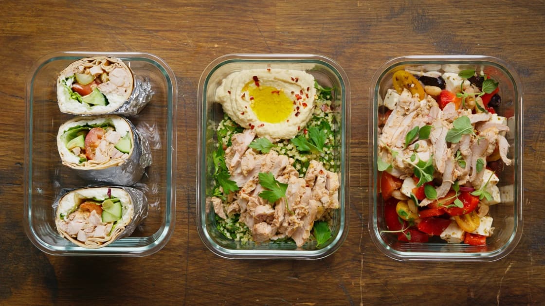 Tre matlådor med olika maträtter står på ett träbord.