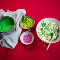 En skål med popcorn och två mindre skålar med godis står bredvid en kastrull på ett bord.