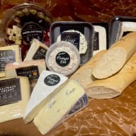 En bricka med olika ostar och pålägg samt två halva baguetter.