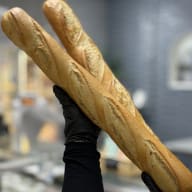 Händer i skyddshandskar håller upp två baguetter i ett bageri.