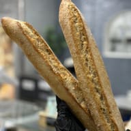 En hand med skyddshandske håller upp två baguetter i ett bageri.