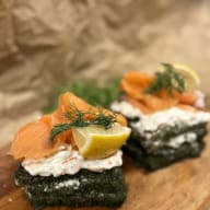 Öppna smörgåsar på tångark med krämig röra, rökt lax, citronskiva och dill på en träbräda.