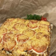 Rektangulär ugnsgratäng täckt med smält ost och tomatskivor på en serveringsbräda.
