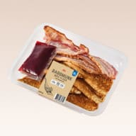 En förpackning med raggmunk, bacon och lingonsylt står på ett underlag.