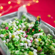 En skål med popcorn och en liten julgransfigur står på ett bord med ljus i bakgrunden.