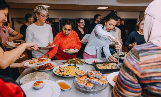 Flera personer står runt ett bord och tar mat från olika fat.