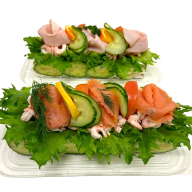 Två öppna smörgåsar toppade med sallad, räkor och gravad lax på plastbrickor.