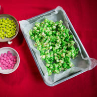 En bricka med popcorn bredvid två skålar med godis på en duk.