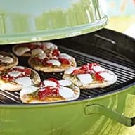 Sex minipizzor som ligger på en grill, locket på grillen är halvt öppet.