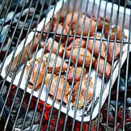 En grillgaller med flera bitar kött som tillagas över glödande kol.