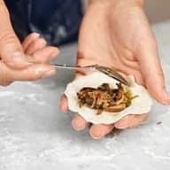 En person håller en dumpling med fyllning och använder en pincett för att justera innehållet.