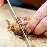 En person skär en lök på en skärbräda med en kniv.