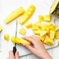 En person skär ananas på en skärbräda med en kniv.