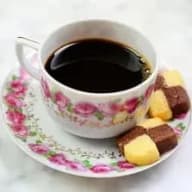 En kopp kaffe står på ett fat med några bitar choklad och frukt bredvid.