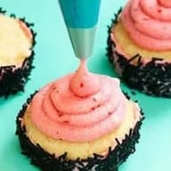 En person dekorerar muffins med frosting från en sprits.