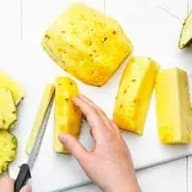 En person skär upp en ananas på en skärbräda med en kniv.