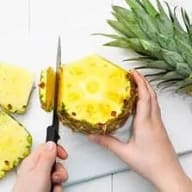 En person skär en ananas med en kniv på ett bord.