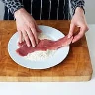 En person lägger en köttbit på en tallrik med mjöl på en skärbräda.