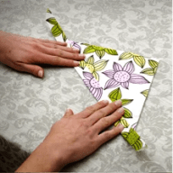 En person viker ett papper med blommönster på en yta med mönstrad bakgrund.