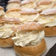 Flera semlor på ett bakplåtspapper, fyllda med riklig vispgrädde.