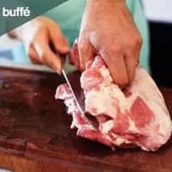 En person skär kött på en skärbräda med en kniv.