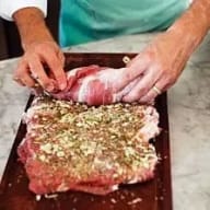 En person förbereder kött på en skärbräda med kryddor.